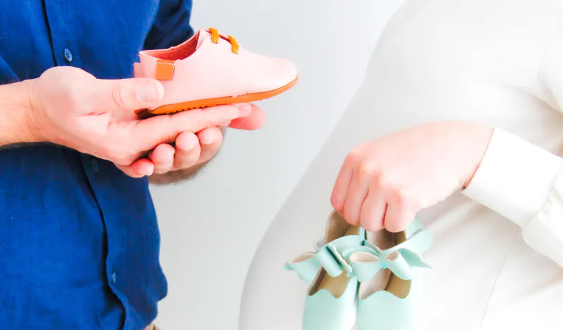 Expecting parents holding pink and blue baby shoes