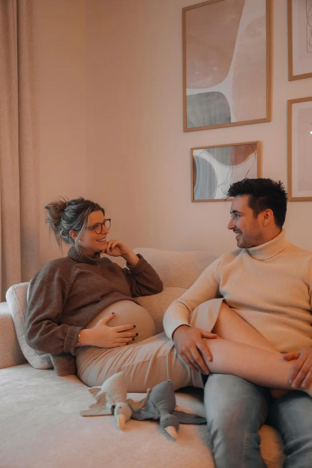 Pregnant couple smiling at each other on a sofa