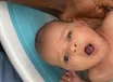 A newborn looking up from a baby bath, a parent’s hand holding their head