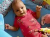 A three-month-old baby in a red floral romper lying on a blue play mat