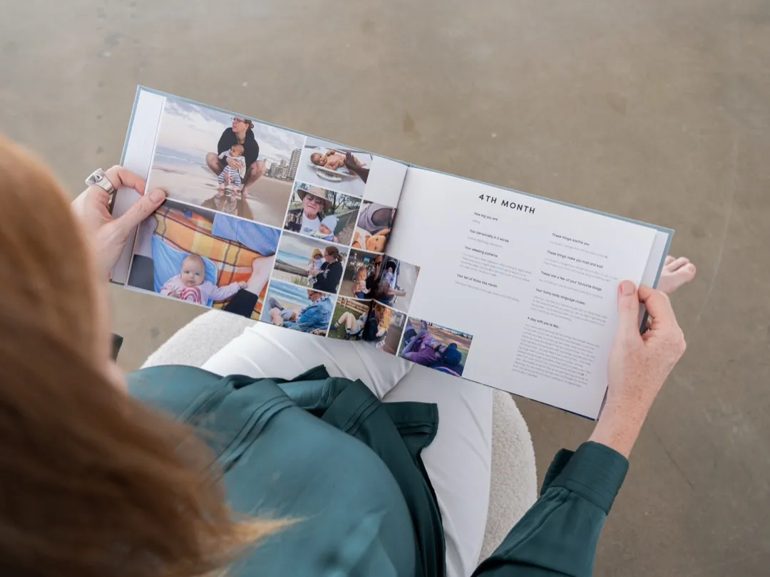 A mother reads through a monthly spread in her Makia baby journal, filled with beach photos and captions.