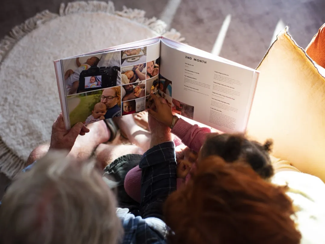 Three generations lean in together to read a page of monthly photos in a finished Makia journal.