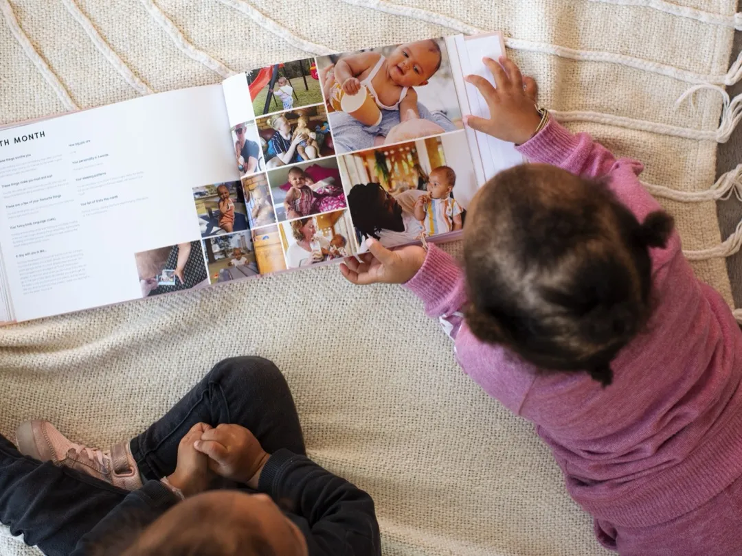 A toddler reaches for the pages of her own baby journal, filled with photos from her first year.