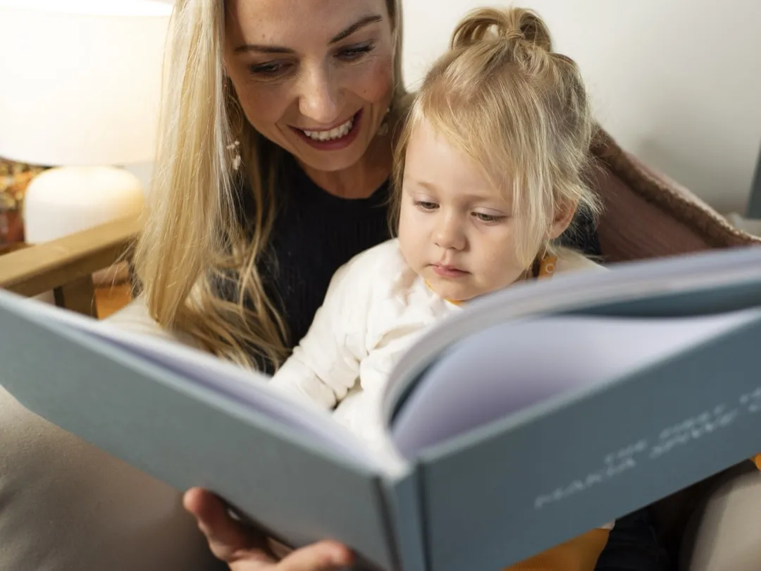 A mother and her toddler smile together while reading their finished, printed Makia journal.