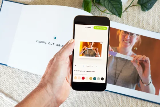 A phone showing the Baby Bump Journal beside its printed Finding out spread