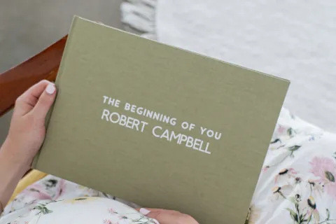 A pregnant parent holding their finished Makia journal, a linen hardcover with the baby's name embossed on the cover